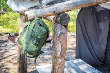 Fototapeta premium Hiking backpack hangs on wooden stick at place to relax in summer forest.