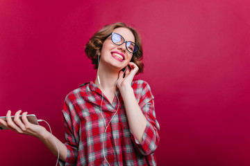 Inspired stylish girl in glasses laughing while listening music on claret background. Studio shot...