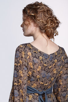 Portrait Of A Young Caucasian Woman With Wavy Hair In Vintage Retro Dress From Back Side