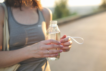 brunette girl with water in glass bottle in park