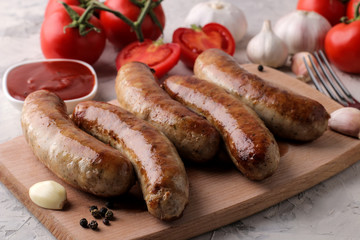 Delicious grilled sausages on a board with red sauce and spices on a light background. B-B-Q.