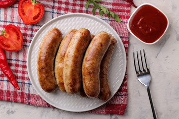 Delicious grilled sausages on a plate with red sauce and spices on a light background. B-B-Q. top view