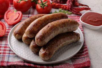 Delicious grilled sausages on a plate with red sauce and spices on a light background. B-B-Q.