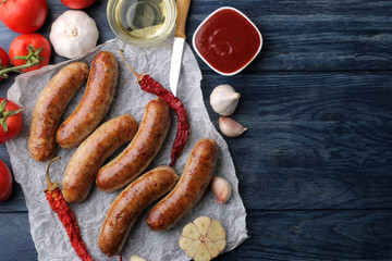 Delicious grilled sausages on paper with red sauce and spices on blue wooden background. B-B-Q. top view