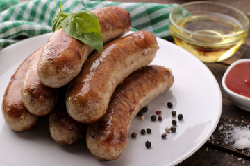 Delicious grilled sausages on a plate with red sauce and spices on a brown wooden background. B-B-Q.