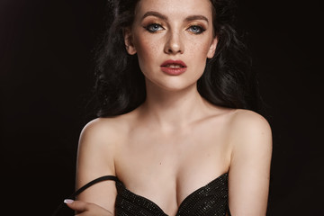 Beautiful brunette girl with clean skin and make-up in black dress on black background. Dramatic portrait. Closeup portrait.