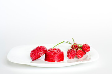 Raspberry jelly on a white plate with raspberry berries on a twig on a white background.