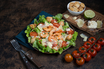 Traditional Caesar salad with shrimp, Parmesan and croutons on a dark wooden background.