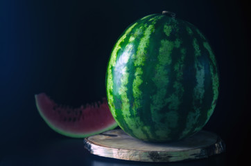 Ripe whole watermelon stands on a wooden board against a black background