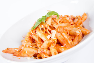 Penne with pesto rosso and sun dried tomatoes decorated with basil on a white background