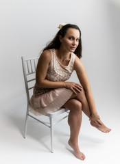 Naklejka premium Horizontal portrait full length sitting on a white chair on a white background beautiful pretty woman in a fashionable light pink dress, in various poses. Stylish trendy youth.