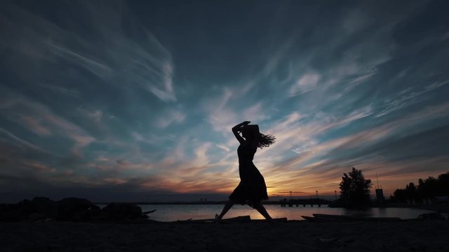 girl dancing beautifully at sunset near the water. silhouette of a graceful ballerina against the sunset sky.