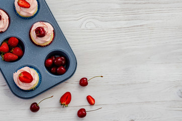 baking tray with fruit and cupcakes on a white wooden background