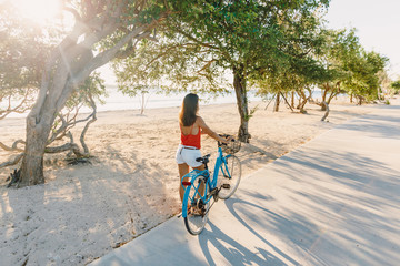 Happy young woman on blue bicycle near ocean in tropical island