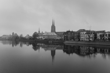 Fototapeta na wymiar Black and white view of the Cathedral of St. John the Baptist reflected in Oder river at cold snowy day. Ostrow Tumski district. Wroclaw. Poland