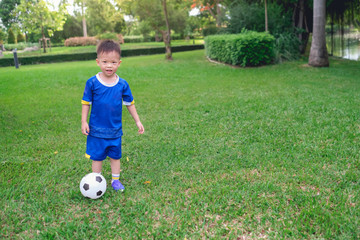 Cute little smiling Asian 3 - 4 years old kindergarten boy, football player in soccer uniform is...
