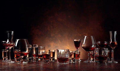 Set of strong alcoholic beverages in glasses on a brown background.