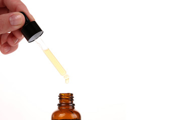 Cosmetic pipette in the hand on white background. Essential oil falling from glass dropper