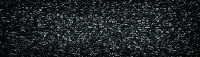 Black crushed granite stone wall wide texture. Angular rock surface panorama. Dark panoramic...