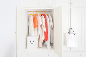 Collection of clothes hanging on rack in white wardrobe in dressing room and two paper shopping bags. Fashion shopping concept background.