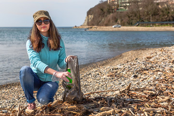 A young woman puts the collected garbage in a bag and posing for the camera. Cleaning of the...