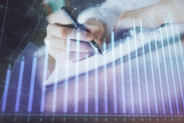 Financial forex graph displayed on hands taking notes background. Concept of research. Double...