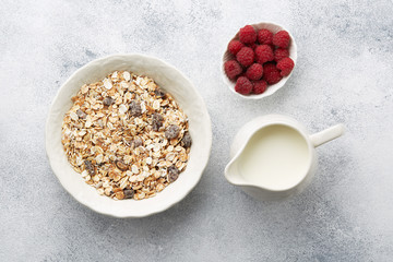 A plate of delicious muesli, a jug of milk and raspberries on the table, top view. Muesli consist of a blend of multigrain flakes with dried fruit, nuts and sunflower seeds.