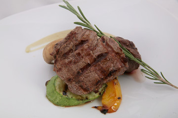 Appetizer steak of medium rarity with rosemary leaves and sauce. On a vegetable pillow close-up on a white background.