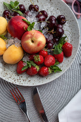 Healthy fruit platter, strawberries, apples, peaches, apricots on a dark gray wooden table, top view, close-up, selective focus.