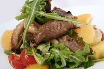 Appetizing salad with meat, cherry tomatoes, orange and arugula. Veal with vegetables on a white background