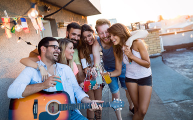 Obraz premium Young friends having fun at a rooftop party, playing the guitar, singing, dancing and drinking