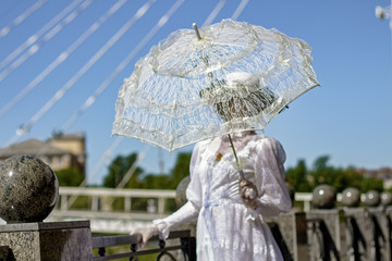 A girl in a long white dress with a hat and an umbrella.