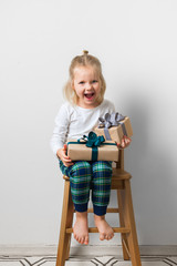 Scandinavian minimalism christmas and new year concept with kid - little girl with stack of gift box on a chair in room