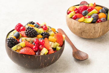 Colourful fruit salad in a coconut bowl and wooden spoon white  stone surface