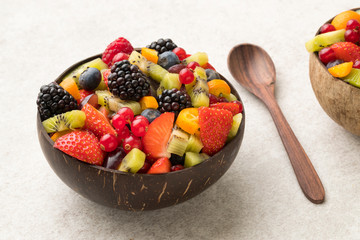 Colourful fruit salad in a coconut bowl and wooden spoon white  stone surface