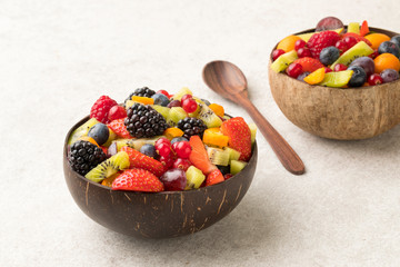 Colourful fruit salad in a coconut bowl and wooden spoon white  stone surface