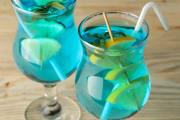 Cocktail blue lagoon in a cocktail glass with lemon and mint on a natural wooden table in the bar....