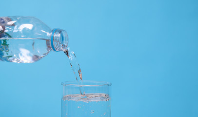 Pouring mineral drinking water from bottle into glass with blue background. 