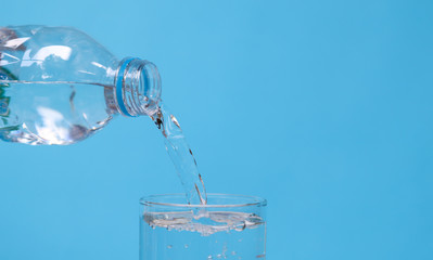 Pouring mineral drinking water from bottle into glass with blue background.
