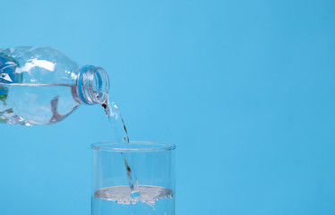 Pouring mineral drinking water from bottle into glass with blue background. 