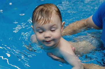 little boy with eyes closed learning to swim in a pool