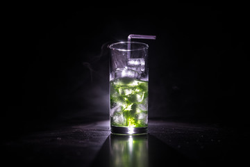 Cocktail glass splashing on dark toned smoky background or colorful cocktail in glass. Party club entertainment. Mixed light.