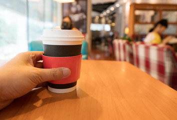 Closeup hand of woman holding the takeaway cup of cappuccino coffee in the cafe