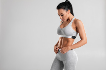 Fitness woman showing abs and flat belly, isolated on gray background. Beautiful athletic girl, shaped abdominal - Powered by Adobe