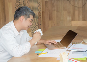 A middle-aged white man sitting in an office with a laptop and holding a coffee mug