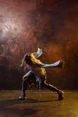 Obraz na płótnie Canvas Photo of young dancing blonde girl in torn blue jeans on brown background in studio