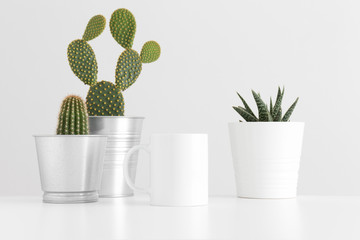 Mug mockup with various types of cactus and a succulent plant on a white table.