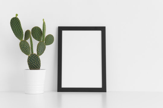 Black frame mockup with a opuntia cactus in a pot on a white table. Portrait orientation.