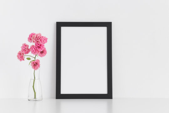 Black frame mockup with pink roses in a glass vase on a white table.Portrait orientation.