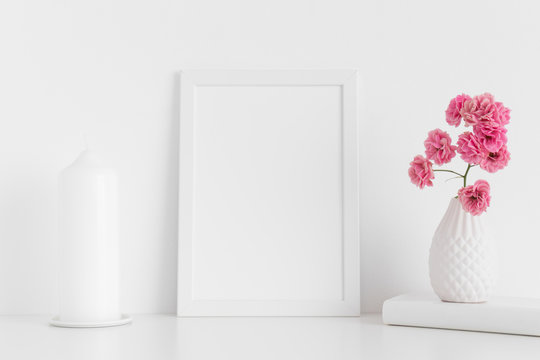 White frame mockup with pink roses in a vase and candle on a white table.Portrait orientation.